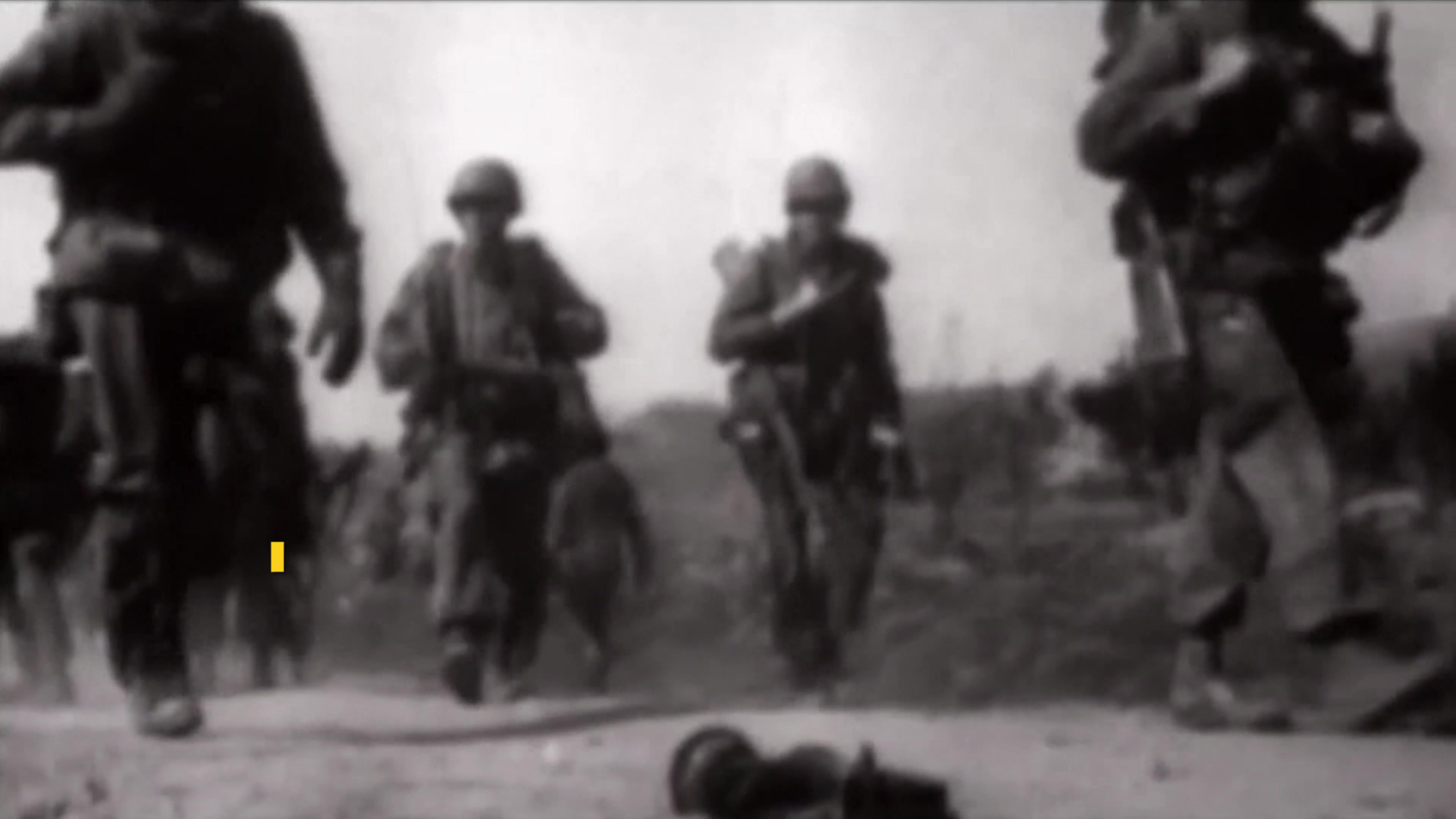 Troops walk on a dirt path in black-and-white video footage.