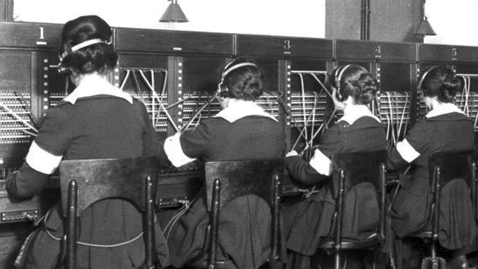 Women, shown from behind, sit in a row at a console.
