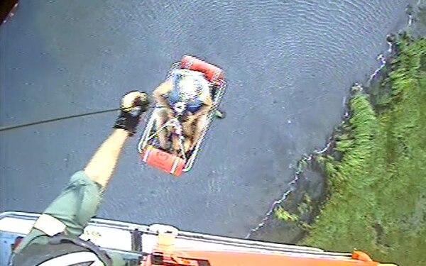 An HH-65 Dolphin helicopter crewmember hoists 2 people from an personal watercraft aground in Grassy Sound, New Jersey, Aug. 30, 2018. The passengers, a 79-year-old grandfather, and his 7-year-old granddaughter were unable to be reached by commercial salvage due to the shallow water that surrounded them.