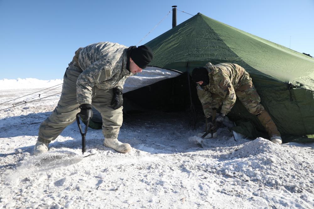 Spc. Brandon Moye and Spc. Garet Sphatt remove snow to protect them against the elements
