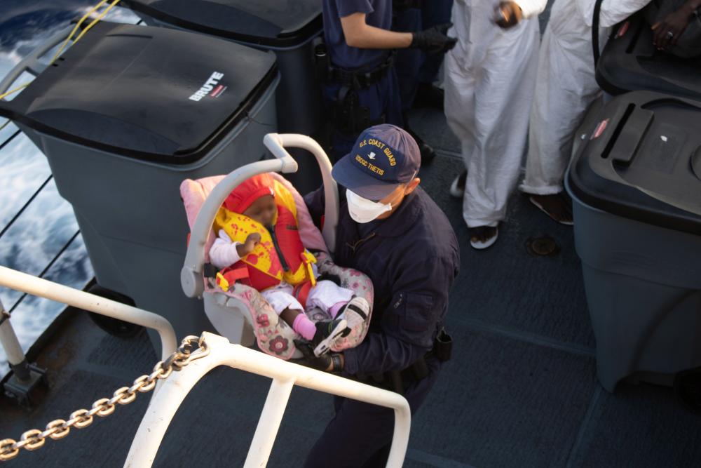 A Coast Guard Cutter Thetis crew member brings a Haitian infant up the stairs of the ship, April 7, 2022. The infant and parent were repatriated to Haiti on April 10, 2022. (U.S. Coast Guard photo by Coast Guard Cutter Thetis crew)