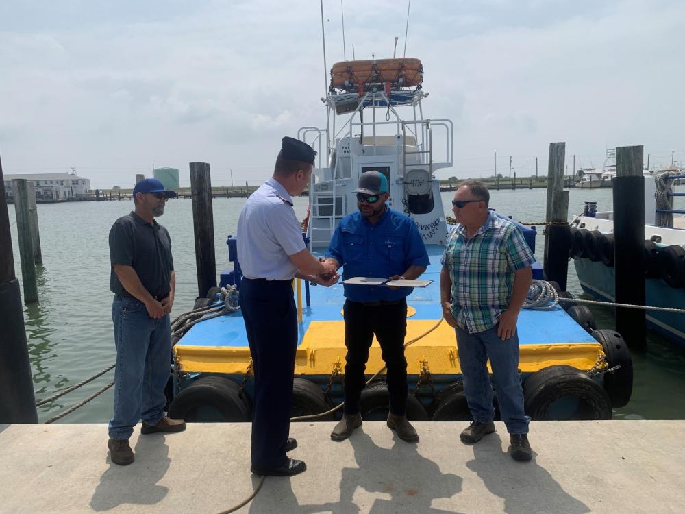 Capt. Hans Govertsen, commander, U.S. Coast Guard Sector/Air Station Corpus Christi, presents a Certificate of Merit to Jonathan Green and the crew of the Tropic Star in Aransas Pass, Texas, May 6, 2022. Green and the crew were presented the award for saving the lives of two individuals who were ejected from their boat in the Brownsville Ship Channel on July 14, 2021. (U.S. Coast Guard photo by Lt. j.g. Darren Hicks)