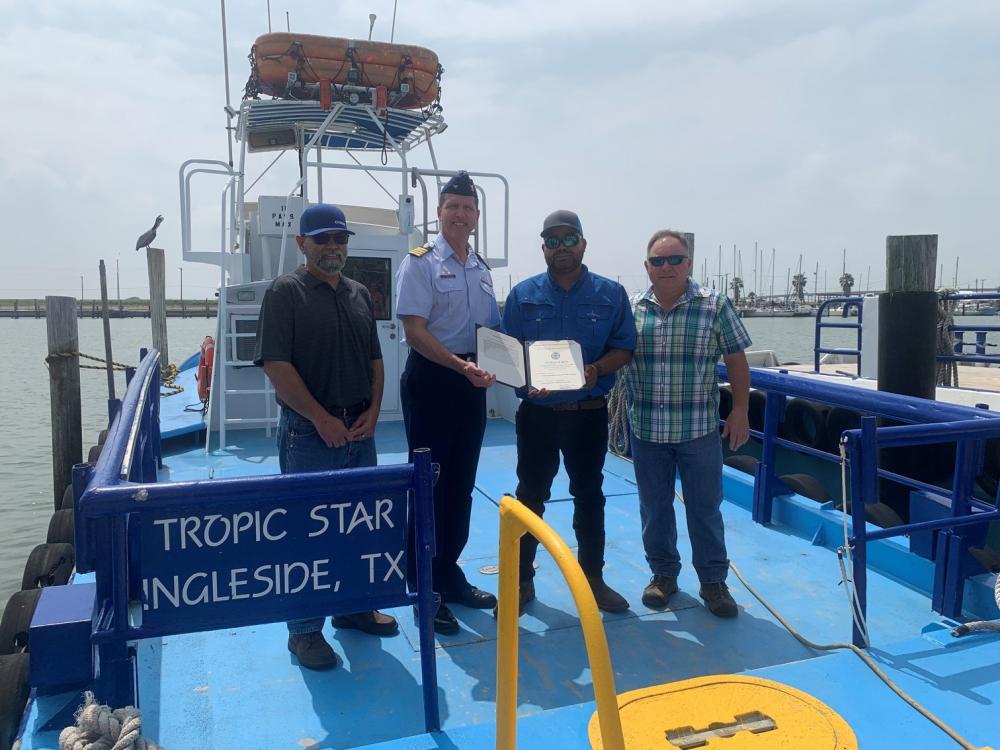 Capt. Hans Govertsen, commander, U.S. Coast Guard Sector/Air Station Corpus Christi, poses for a photo after presenting a Certificate of Merit to Jonathan Green and the crew of the Tropic Star in Aransas Pass, Texas, May 6, 2022. Green and the crew were presented the award for saving the lives of two individuals who were ejected from their boat in the Brownsville Ship Channel on July 14, 2021. (U.S. Coast Guard photo by Lt. j.g. Darren Hicks)