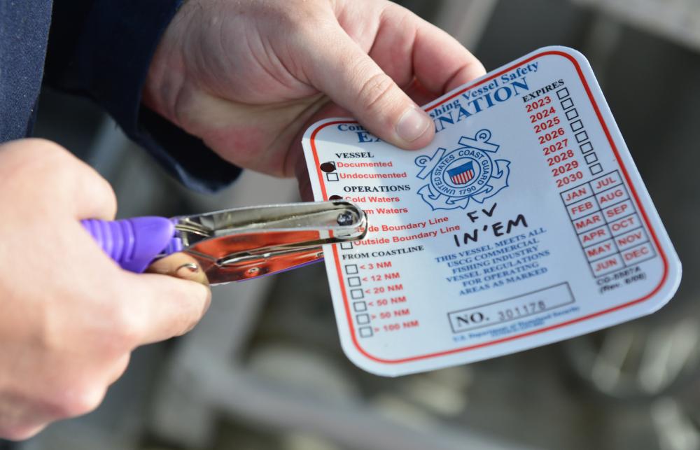 A marine inspector with Coast Guard Sector Anchorage issues a decal to fishing vessel In’Em indicating that it passed a commercial fishing vessel safety exam in Naknek, Alaska, June 16, 2022. Displaying the decal communicates to Coast Guard law enforcement officers on the water that the vessel is in compliance with federal safety laws. U. S. Coast Guard photo by Petty Officer 2nd Class Melissa E. F. McKenzie.