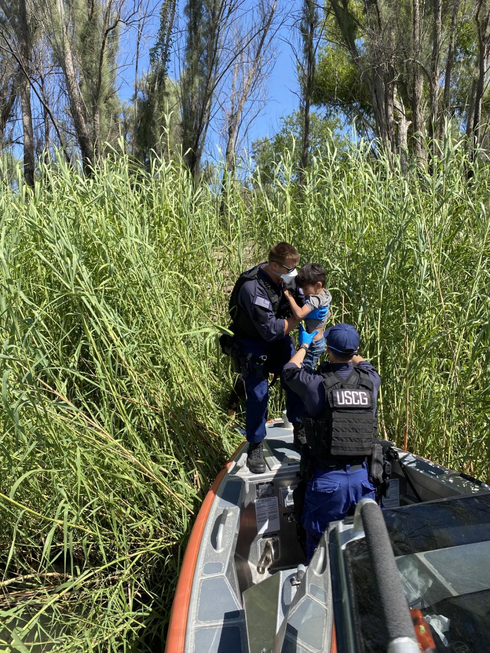 Members from Coast Guard Maritime Safety & Security Team Houston lift a child from the reeds on the U.S. riverbank of the Rio Grande, July 7, 2022. The boy and his mother, two non-citizens who crossed the river, got stranded and signaled for the Coast Guard crew’s help. (U.S. Coast Guard photo, courtesy Maritime Safety & Security Team Houston)