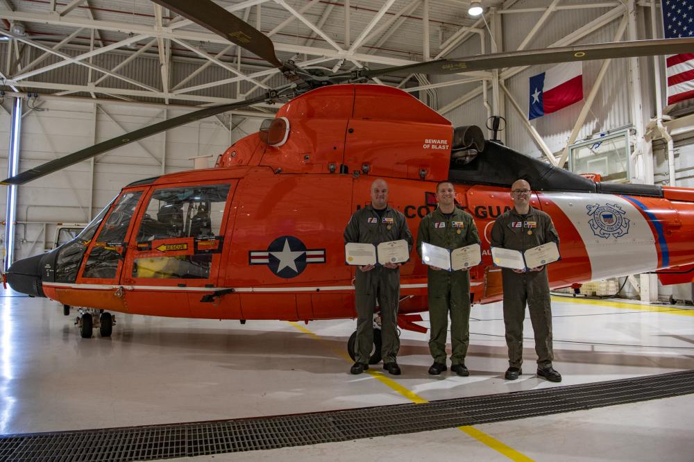 Cmdr. James Conner, an MH-65 Dolphin helicopter pilot, Petty Officer 1st Class Vincent Neiman, an aviation survival technician, and Petty Officer 2nd Class Christopher Collins, an aviation maintenance technician, pose for a photo after reciving Air Medals during an award ceremony at Coast Guard Air Station Houston, Texas, Aug. 19, 2022. During the ceremony, Rear Adm. Richard V. Timme, commander, Coast Guard District Eight, presented Conner, Neiman and Collins with Air Medals for rescuing nine trapped crew members from the Pride Wisconsin, a decommissioned mobile offshore drilling unit that caught fire in Sabine Pass, Texas, on Feb. 24, 2022. (U.S. Coast Guard photo by Petty Officer 2nd Class Ryan Dickinson)
