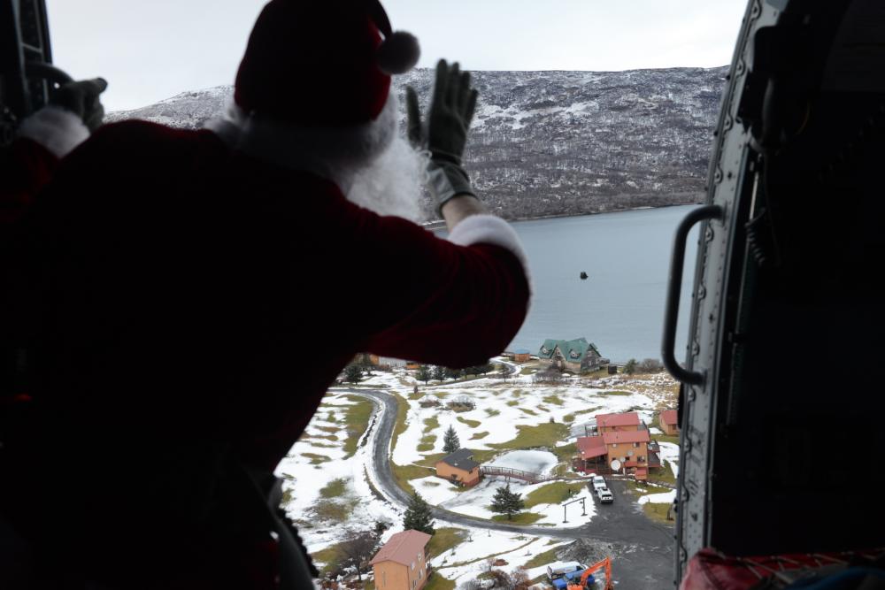 U.S. Coast Guard Petty Officer 3rd Class Chase Burningham, a Marine Science Technician who works at Air Station Kodiak, dressed as Santa Claus, waves aboard a helicopter as it circles over Larsen Bay, Alaska, on Dec. 5, 2022. Burningham volunteered to dress as Santa in support of the annual Santa to the Villages program, which is coordinated by members of the Spouse's Association of Kodiak. U.S. Coast Guard photo by Petty Officer 1st Class Ali Blackburn.