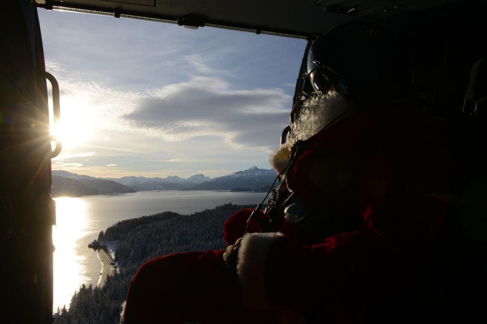 U.S. Coast Guard Petty Officer 1st Class Jason Flynt, an Aviation Survival Technician at Air Station Kodiak, looks out the door of an MH-60 Jayhawk helicopter during a flight to Port Lions, Alaska, on Nov. 30, 2022. Santa, an air station volunteer, dresses up and delivers presents, fresh fruit, and hygiene products alongside members of the Spouse's Association of Kodiak every year since 1976. U.S. Coast Guard photo by Petty Officer 1st Class Ali Blackburn.